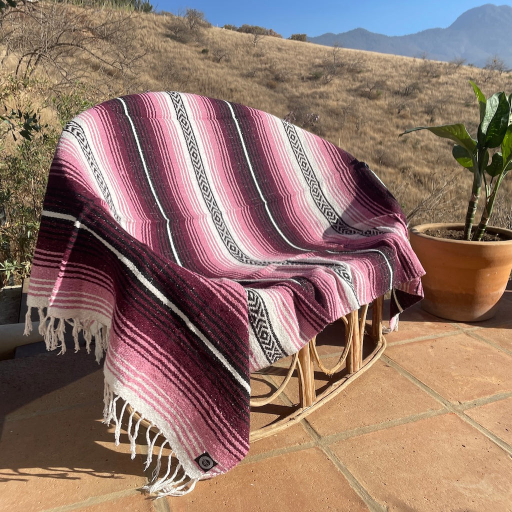 pink, burgunday, and white mexican blanket on a porch